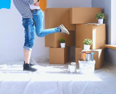 Image showing legs of a man holding a woman with moving boxes and plants in the background.
